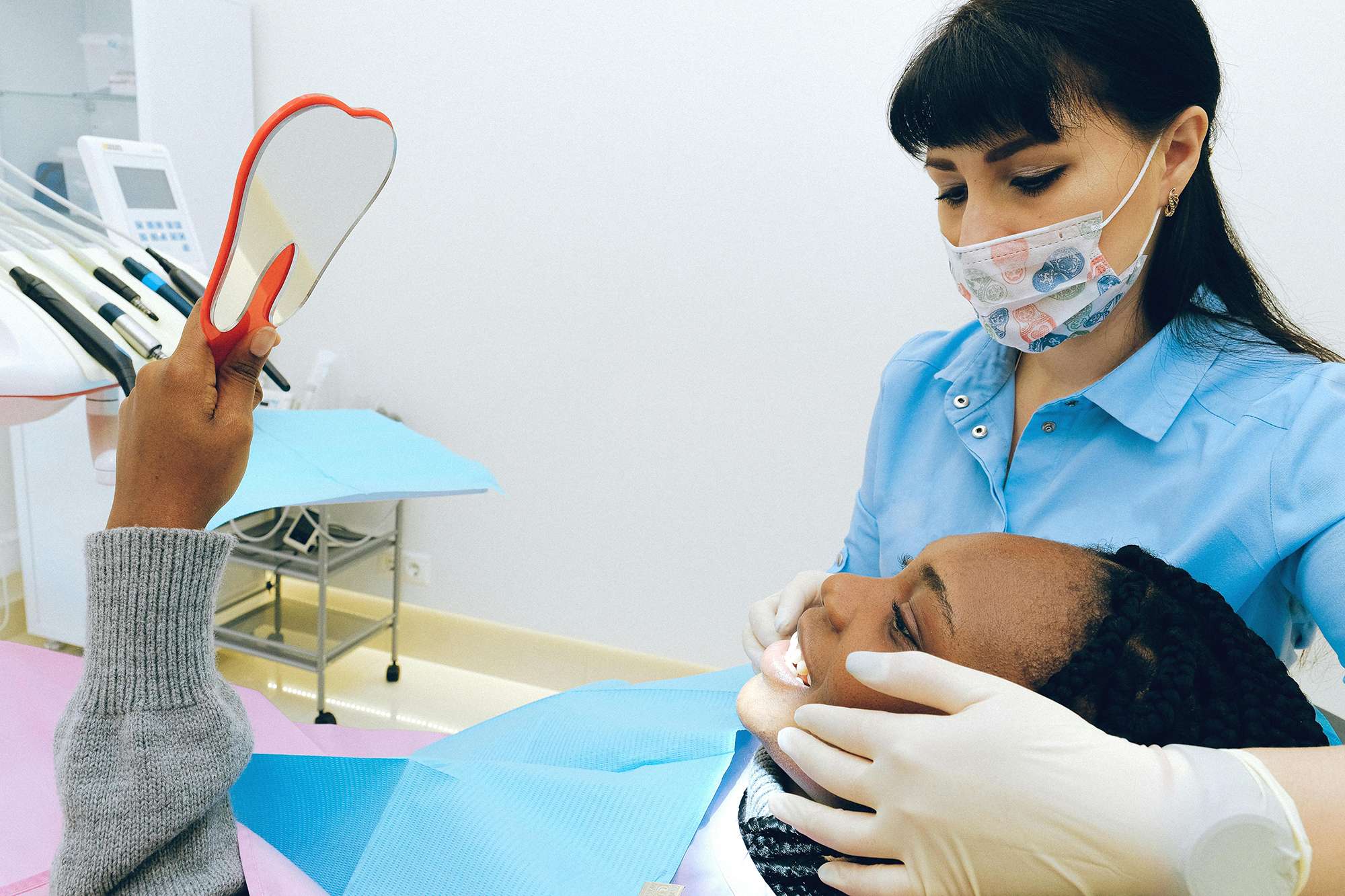 A patient in a dentist's chair looking in a mirror at her teeth as the dentist holds her smile.