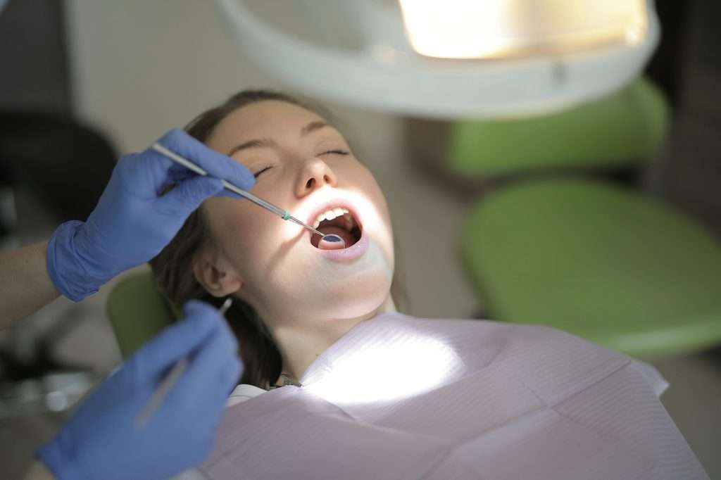 A dentist working on a patient in the dentist's chair, holding a dental mirror to her teeth.