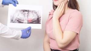 A woman holding the left side of her jaw while a dentist speaks to her about the pain she is having.